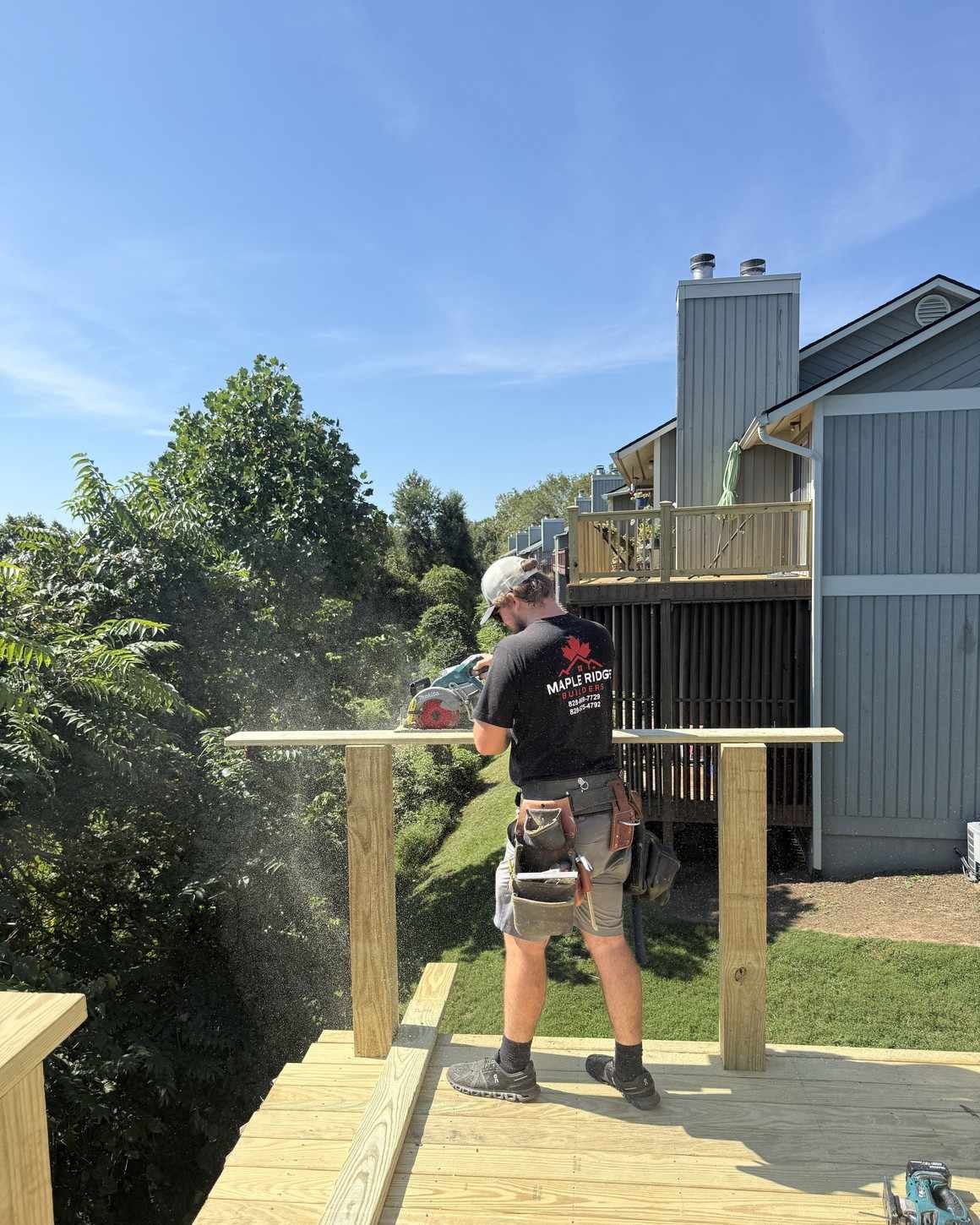 Maple Ridge Builders crew member in a branded shirt cutting deck boards with a circular saw on a new pressure-treated deck