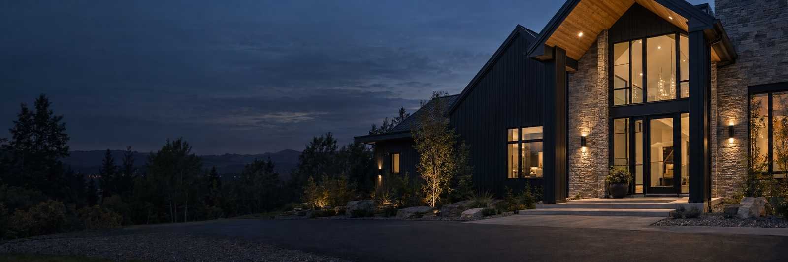 Modern dark-sided home with a stone entry glowing at dusk above a Blue Ridge valley