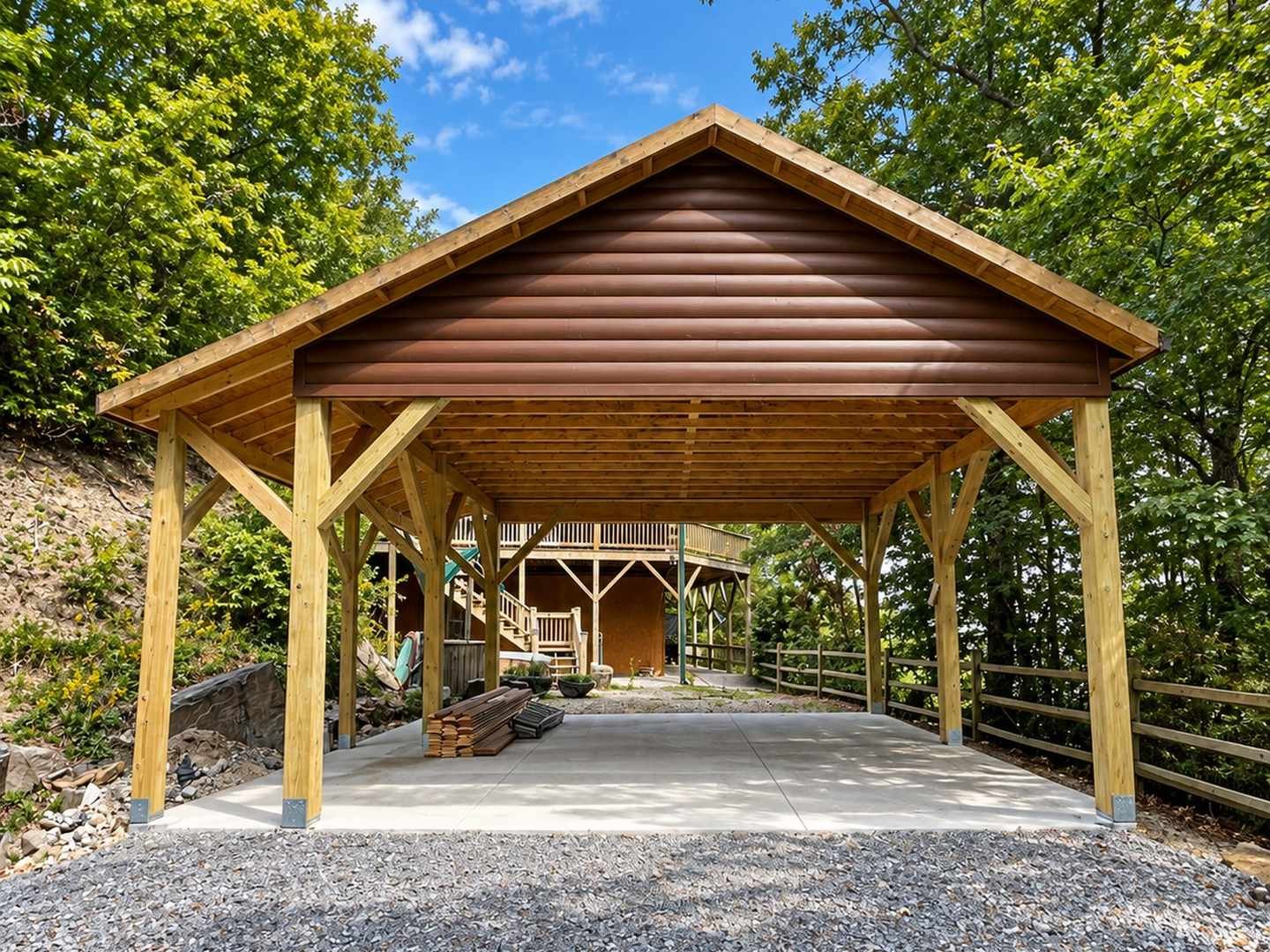 Timber-frame pavilion with exposed posts, rafters, and knee braces over a poured concrete pad