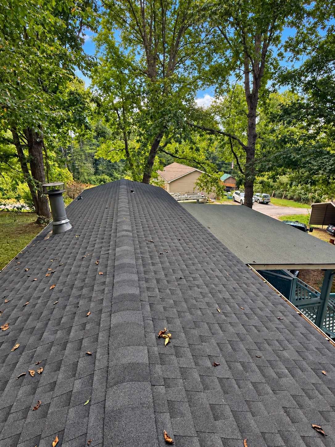 Newly installed charcoal architectural shingle roof seen along the ridge line, framed by green trees